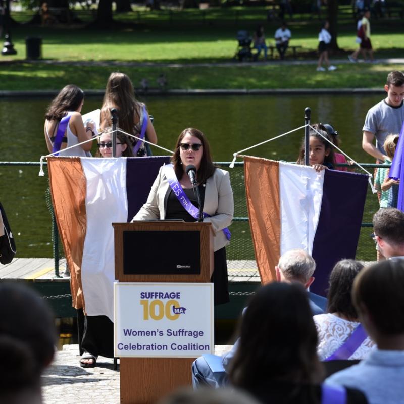 Woman wearing purple sash speaking at podium.