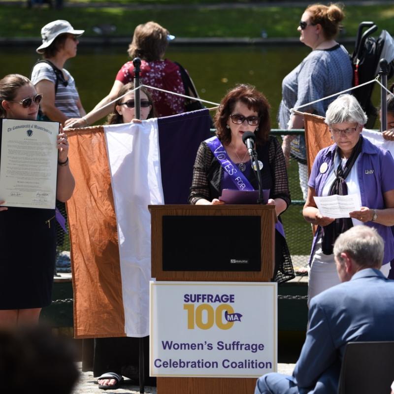 Woman stands at podium speaking.