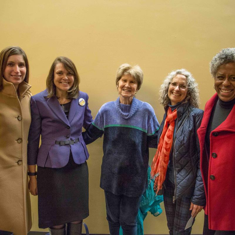 Five women stand indoors smiling.