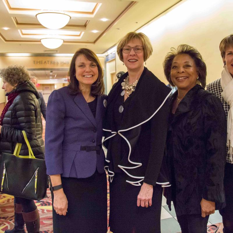 Four women stand indoors smiling.