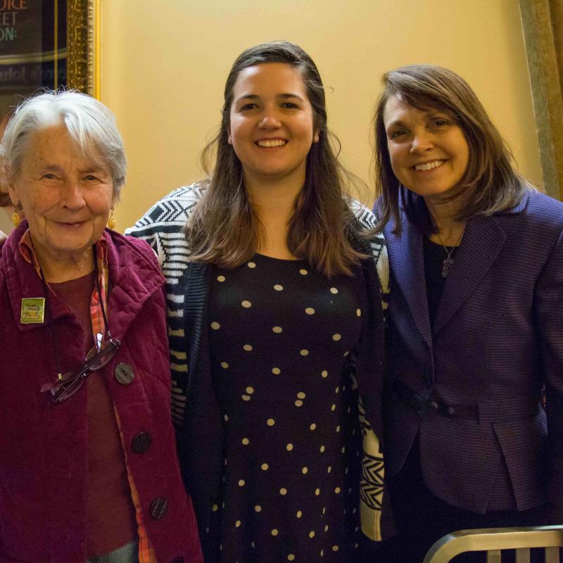 Three women stand indoors smiling.