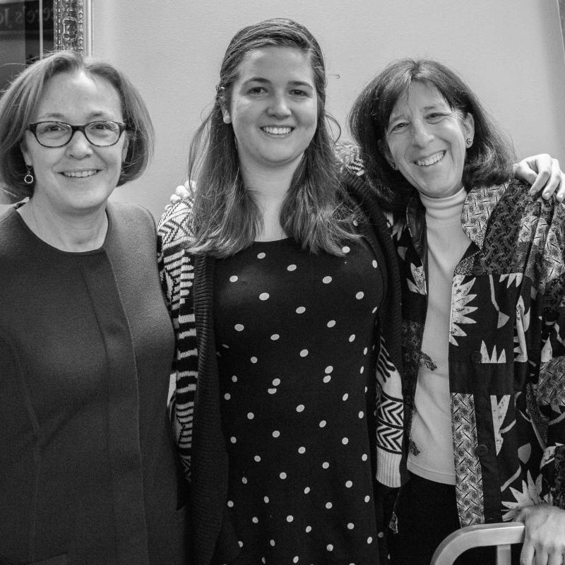 Three women stand indoors smiling.