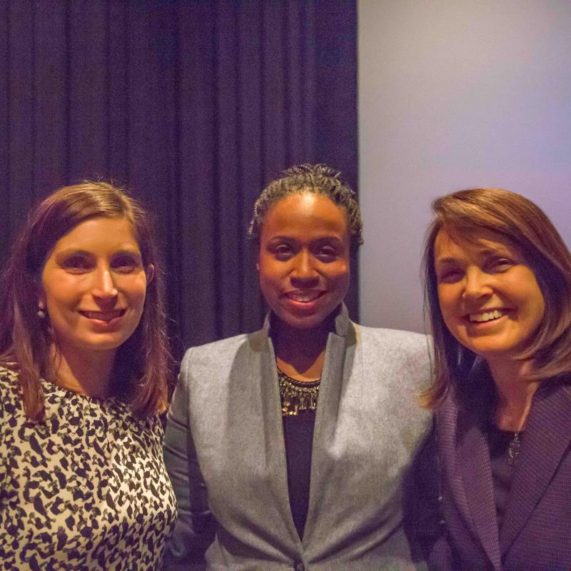 Three women stand indoors smiling.