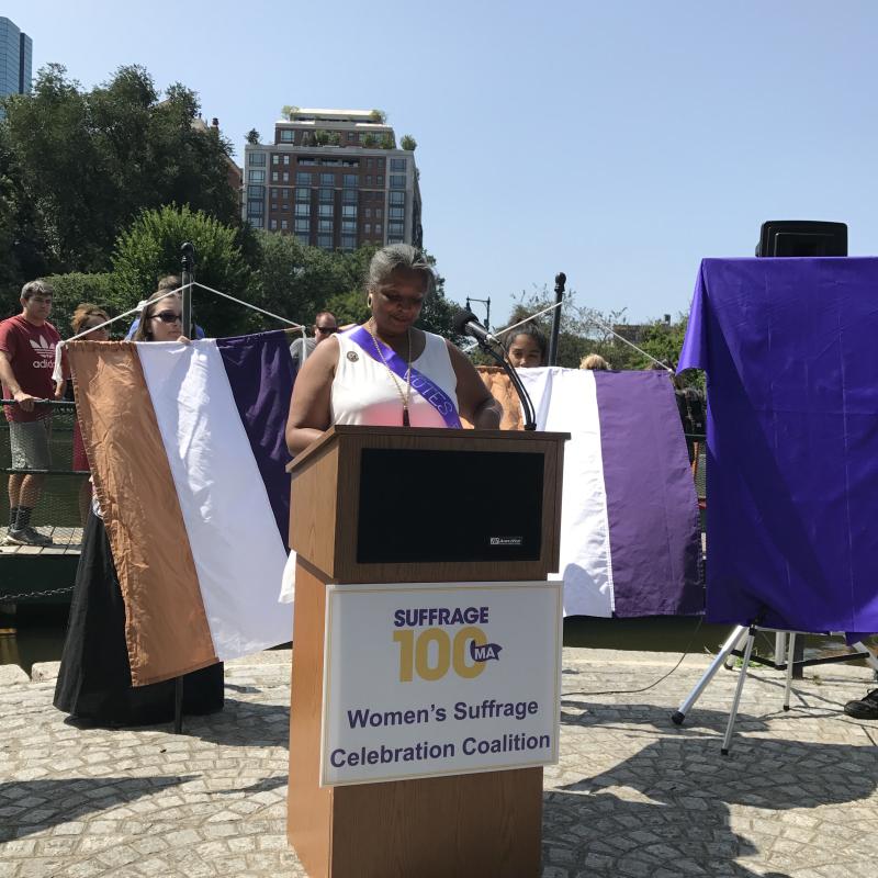 Woman wearing purple sash stands at podium.