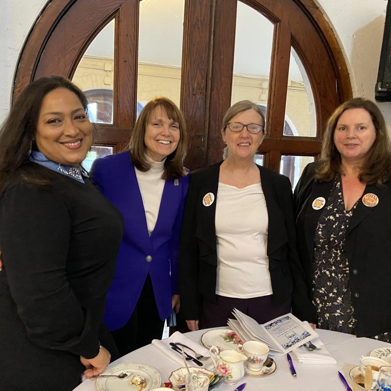 Four women stand indoors smiling.