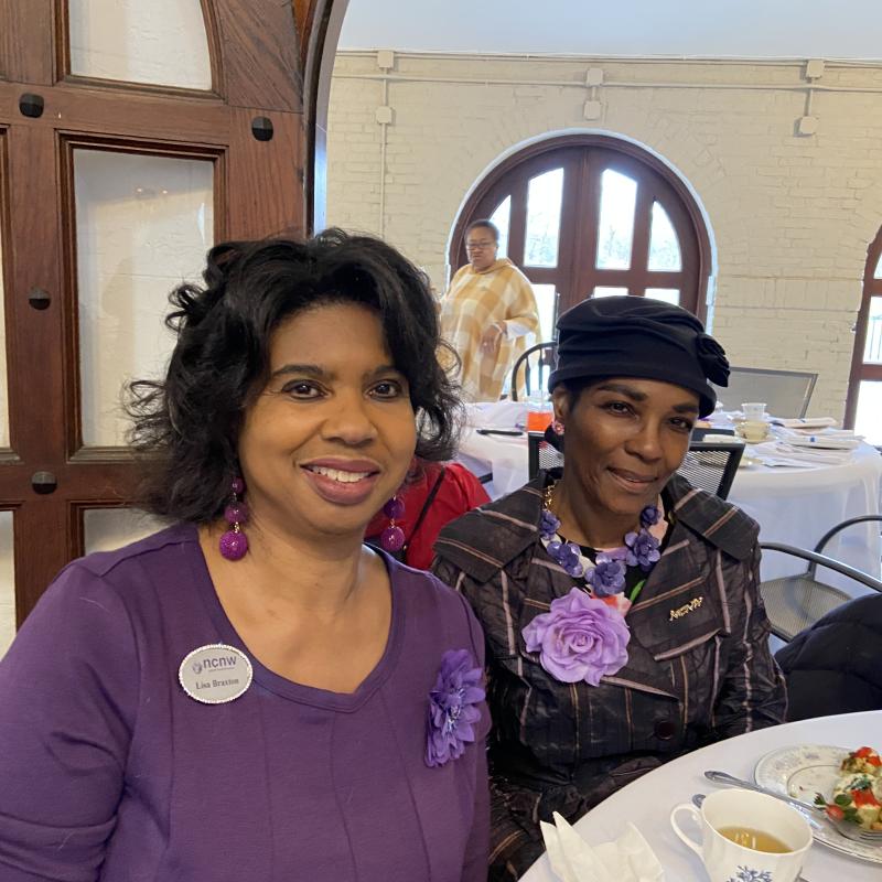 Two women sit indoors smiling.