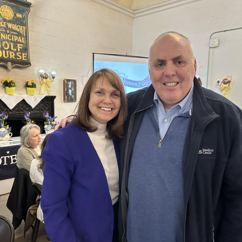 Woman and man stand indoors smiling.