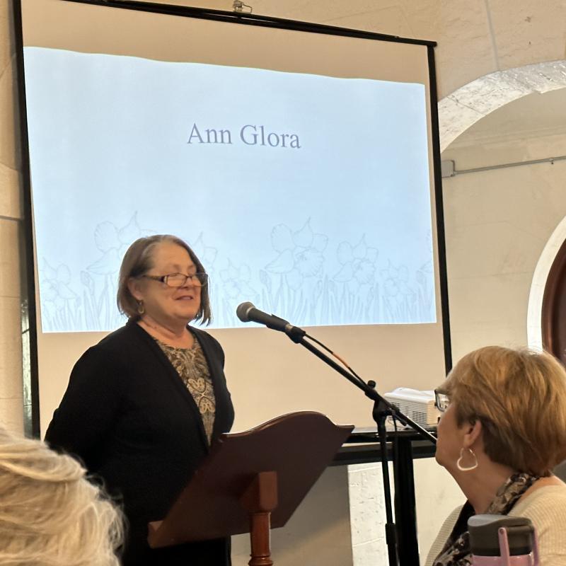 Woman stands indoors speaking at podium.