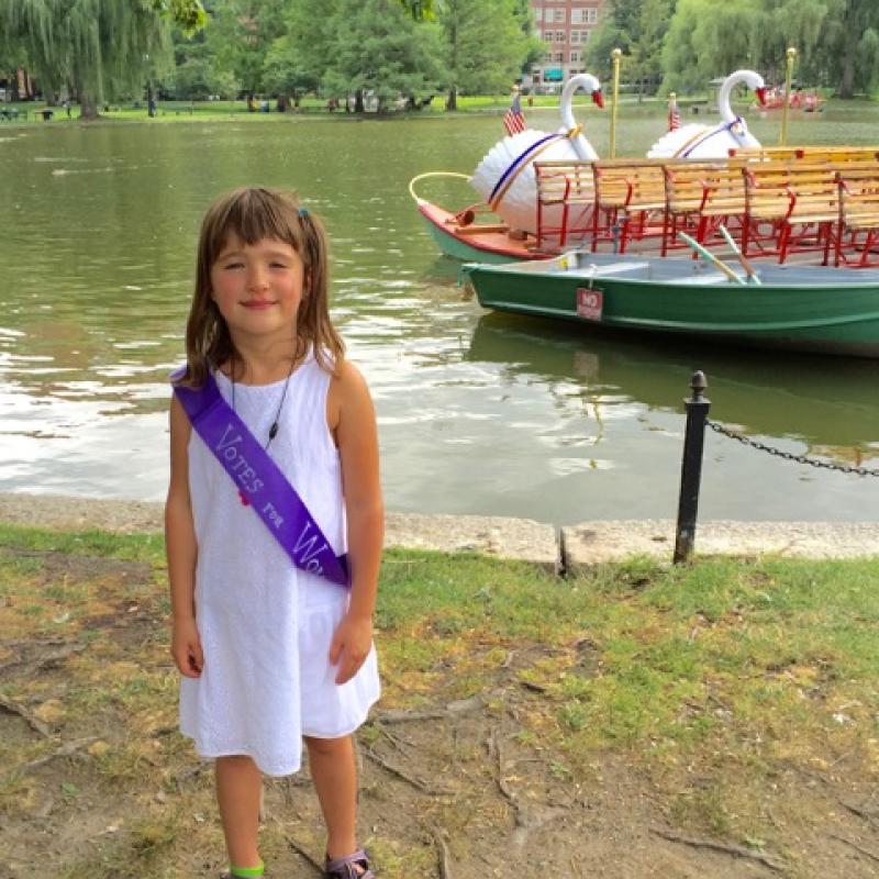 Girl wearing purple sash stands outside.