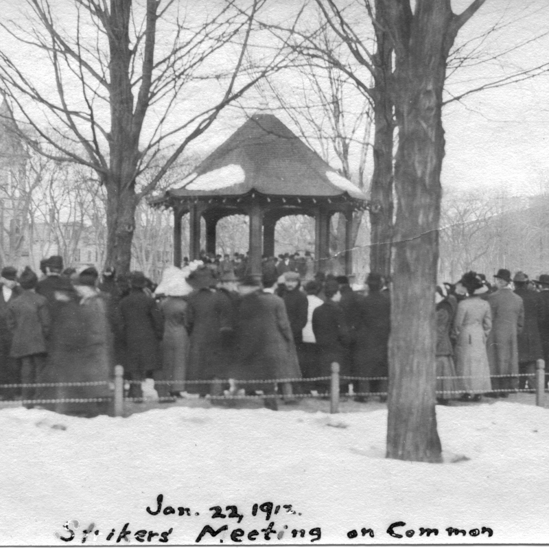 a winter scene of a group of people standing on a common, around a gazebo.