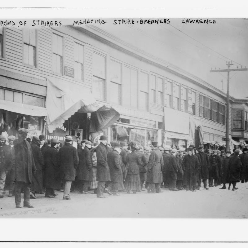 Black and white photograph of crowd outdoors with written text, "Crowd of strikers menacing strike-breakers, Lawrence."