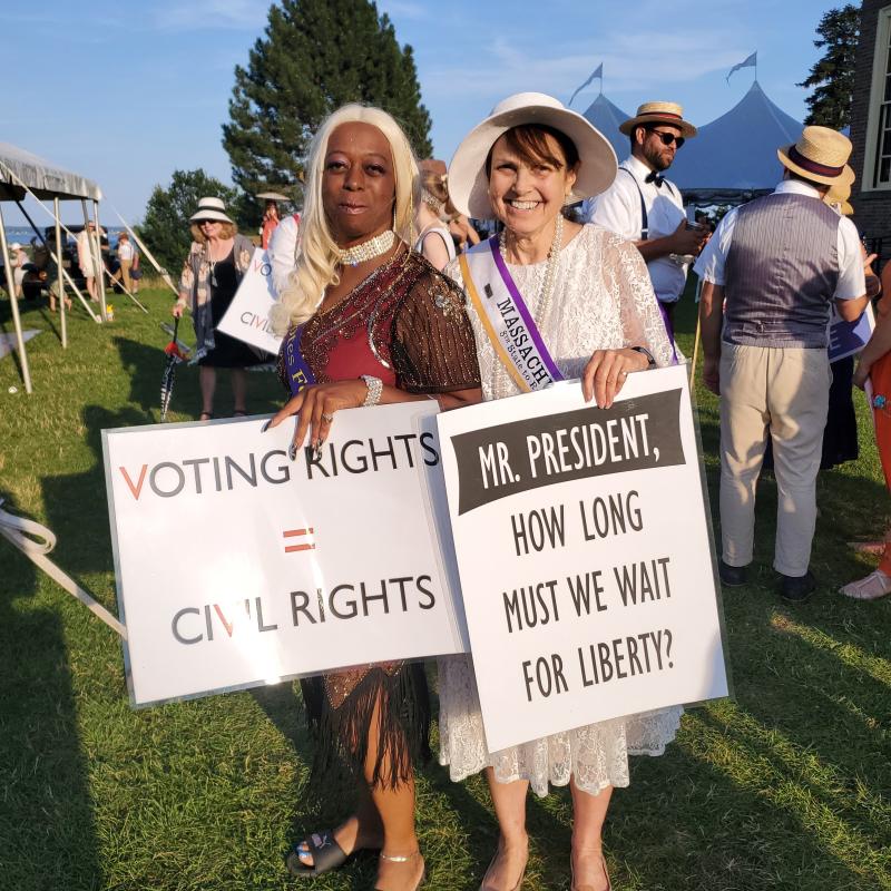 Two women stand outside holding signs.