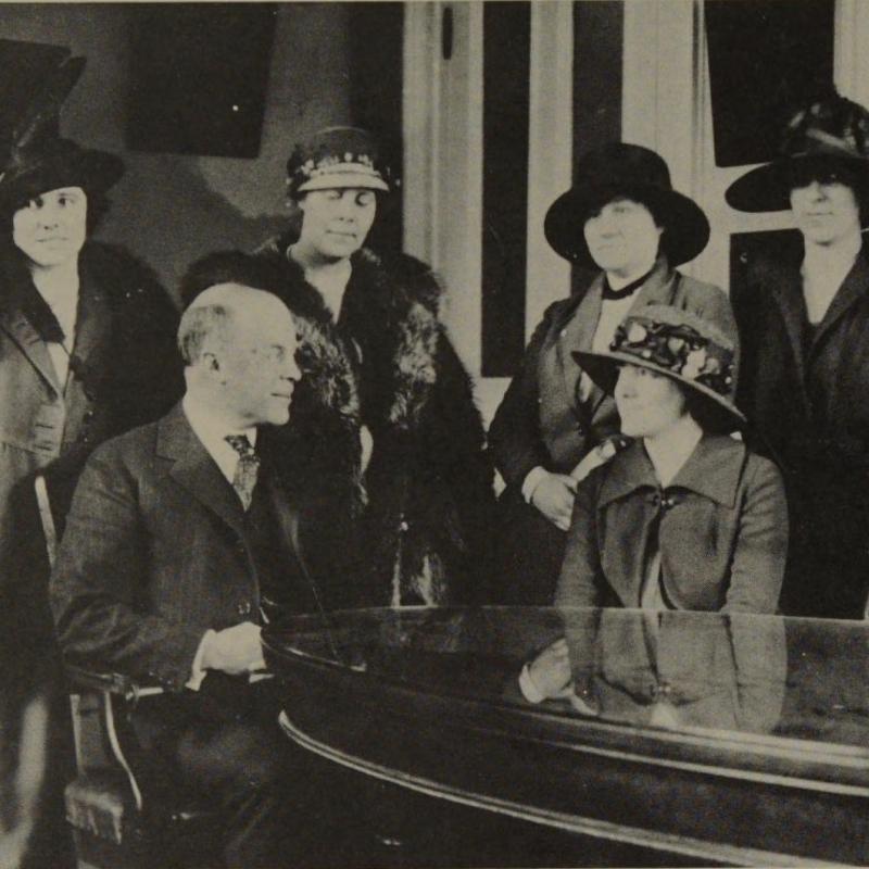 Vintage black and white photo of five women and one man gathered around table.