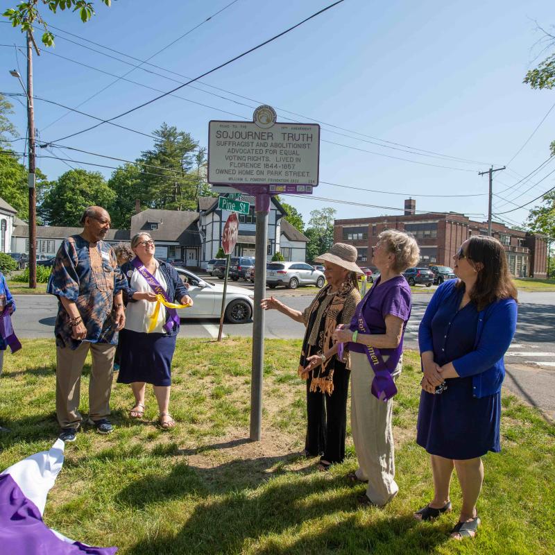 Crowd of people stand outside looking at white and purple Sojourner Truth women's suffrage marker.