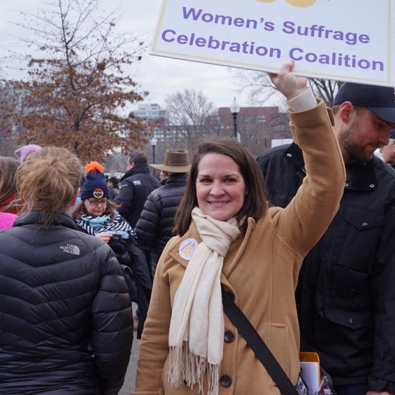 Woman holds Suffrage100MA sign.