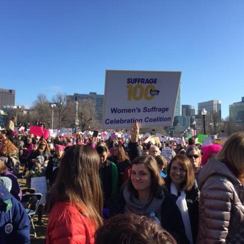 Women hold Suffrage100MA signs in crowd.