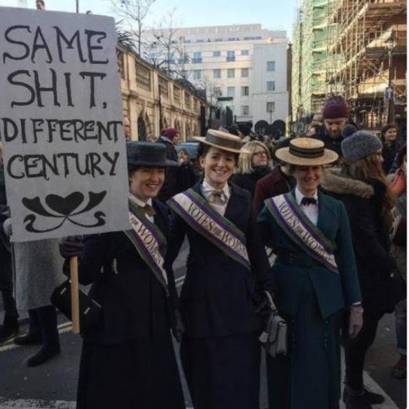 Women hold protest signs in vintage clothes.