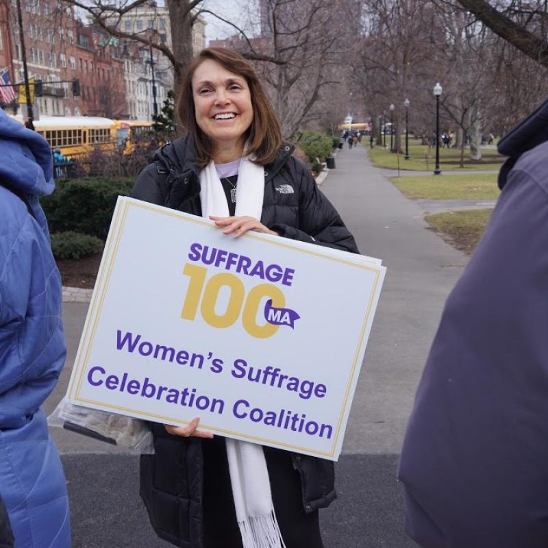 Woman holds Suffrage100MA sign.