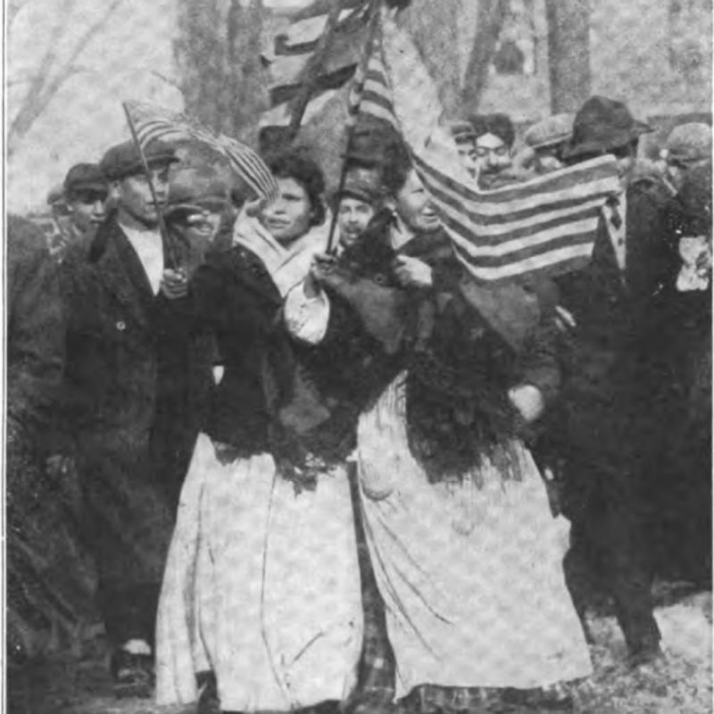 Old photograph of two women marching outdoors and waving American flags.