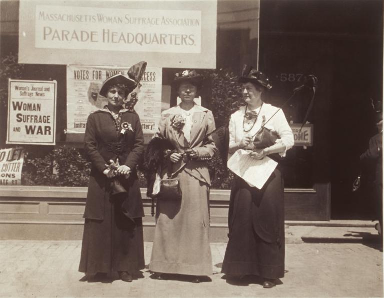 Black and white photograph of three women standing in front of the Massachusetts Woman Suffrage Association Parade Headquarters