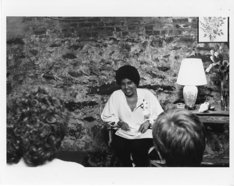 Black and white photograph of Beverly Smith, seated, in front of a stone and brick wall