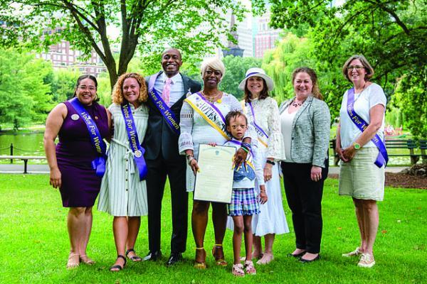 Seven adults and one child stand outside, wearing purple sashes.