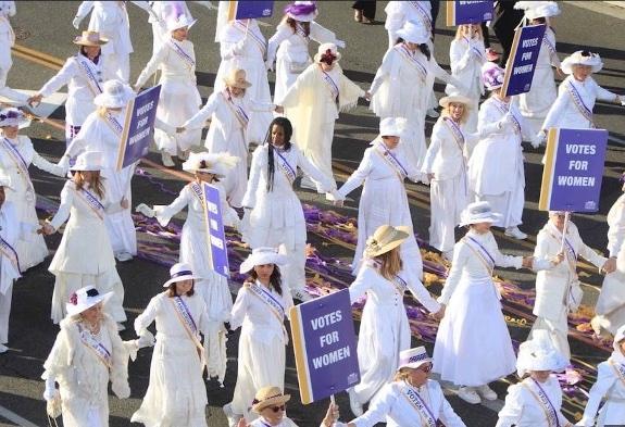 Women in white march in parade.