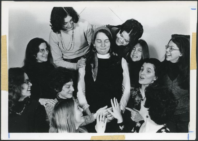 Black and white photograph of 10 women surrounding 1 pregnant woman with their hands on her abdomen.