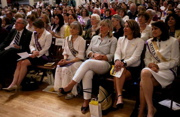 Women in white sit in audience.