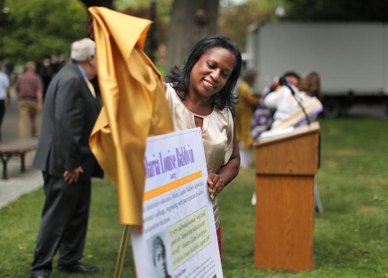 Woman pulls yellow cloth off of sign.