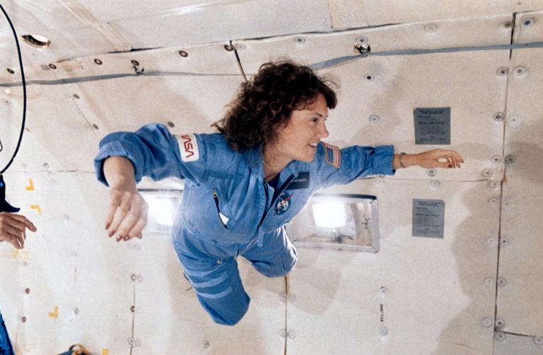 Woman in flight suit floats inside aircraft.