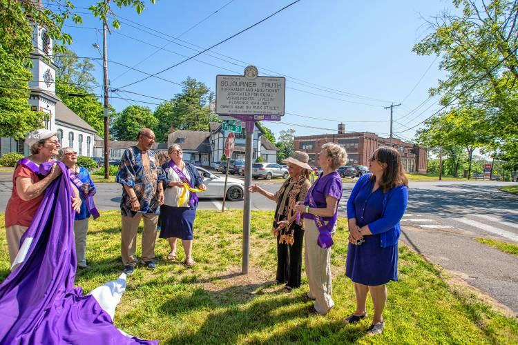 People stand outside next to purple and white sign.