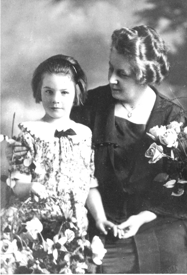 woman sitting with a young girl. Both wear dresses.