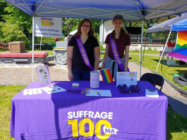 Two teens stand at purple table smiling.