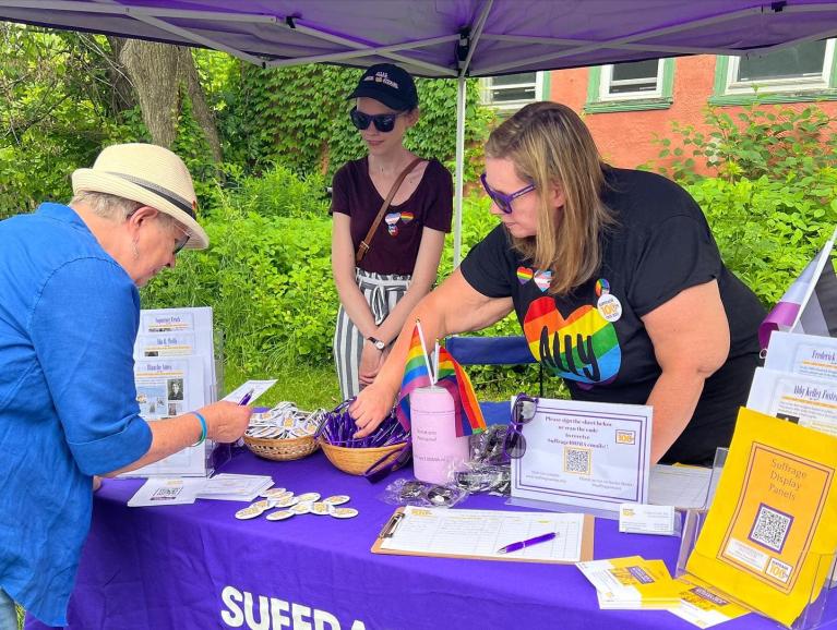 Two women stand at purple table.