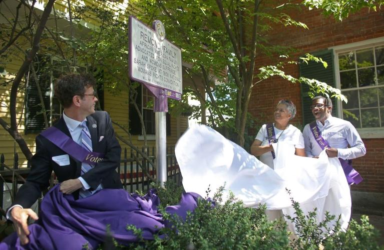 People stand outside next to purple and white sign.