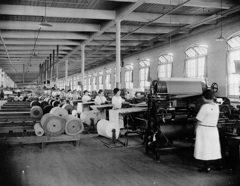 interior of a factory building, with a row of women working at textile machines