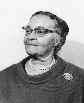 Portrait of a woman wearing glasses and a flower brooch from the shoulders up