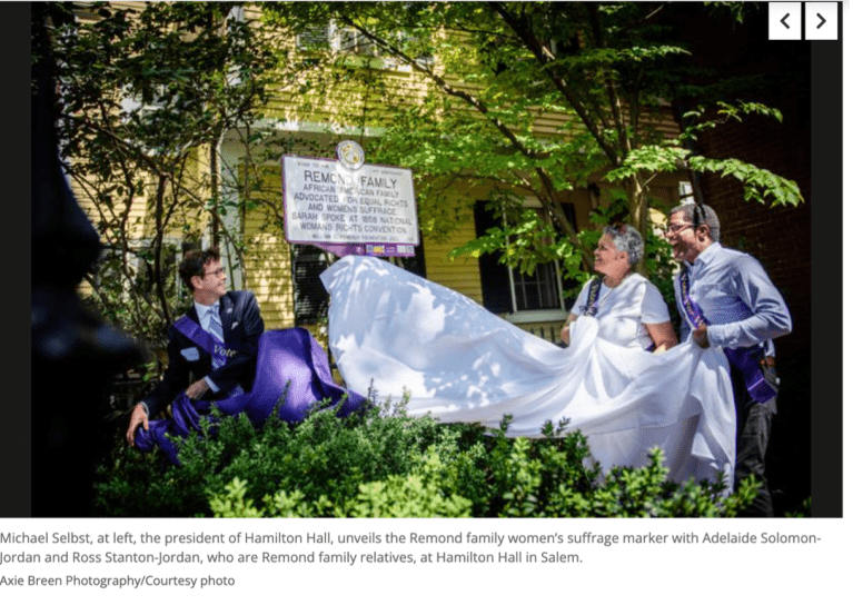 Three people pull cover off white and purple sign.