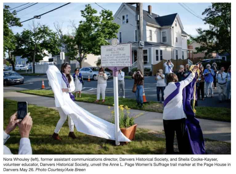 Two women wearing purple sashes stand outside smiling.