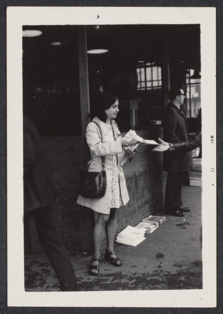 Woman holding newspaper in front of building.