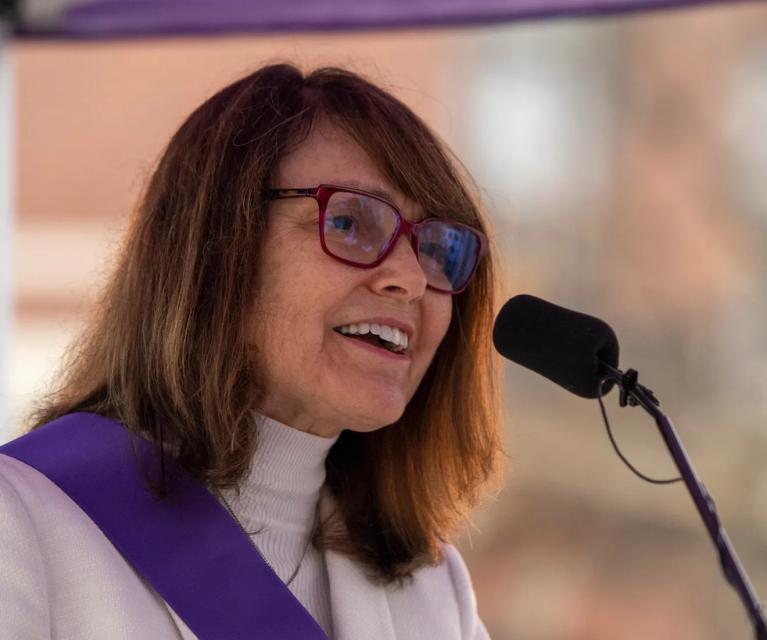 Woman stands at podium speaking.